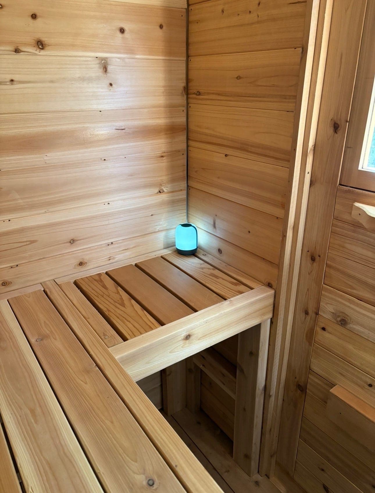 Inside the portable sauna, looking across the L-shaped upper bench and the lower step bench, walls clad in horizontal cedar