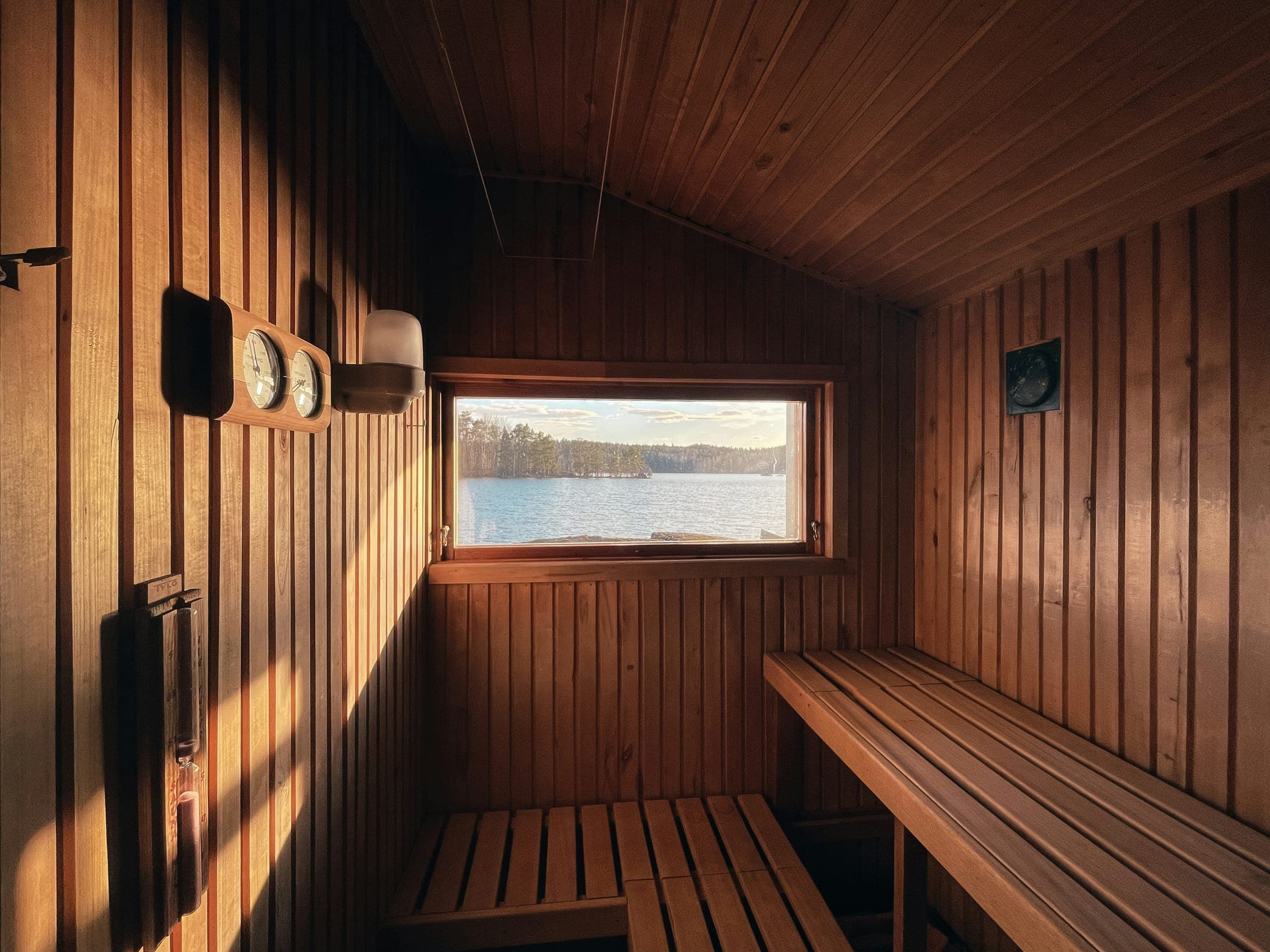 A traditional sauna interior with a long window looking out over a lake at golden hour